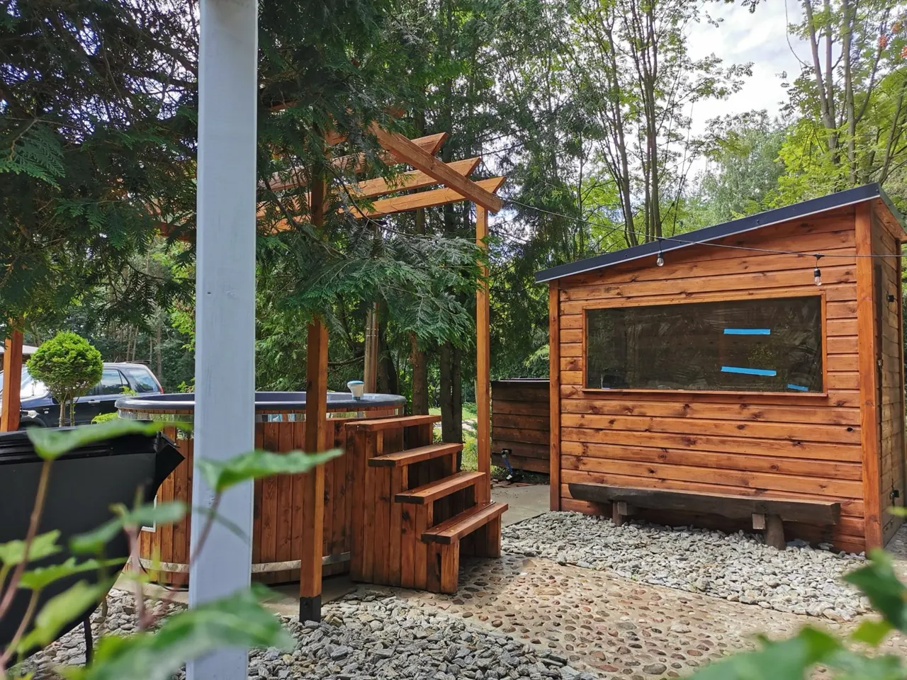 Balia ze schodkami pod pergolą i drewniana sauna w ogrodzie